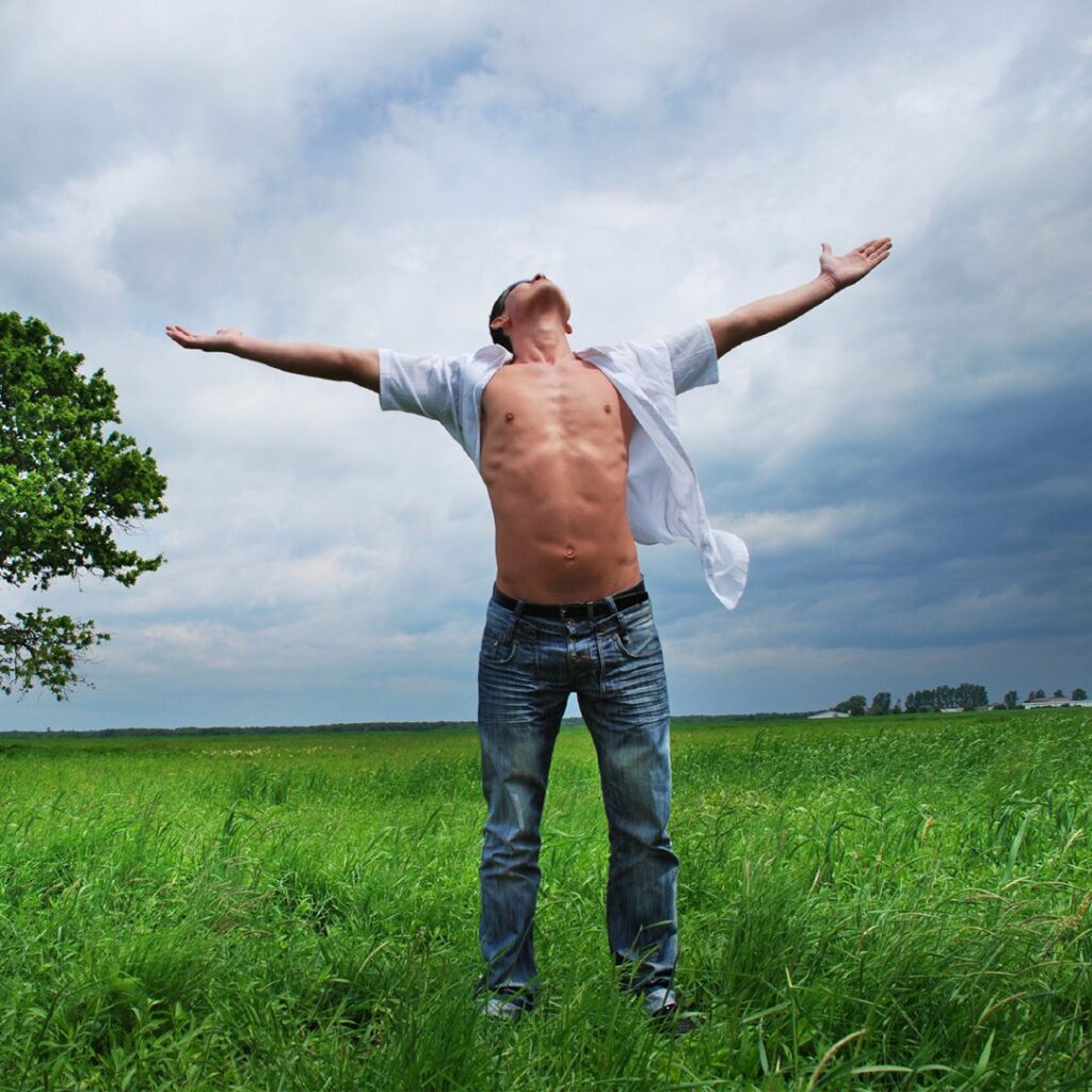 Man with arms outstretched in a green field under a cloudy sky